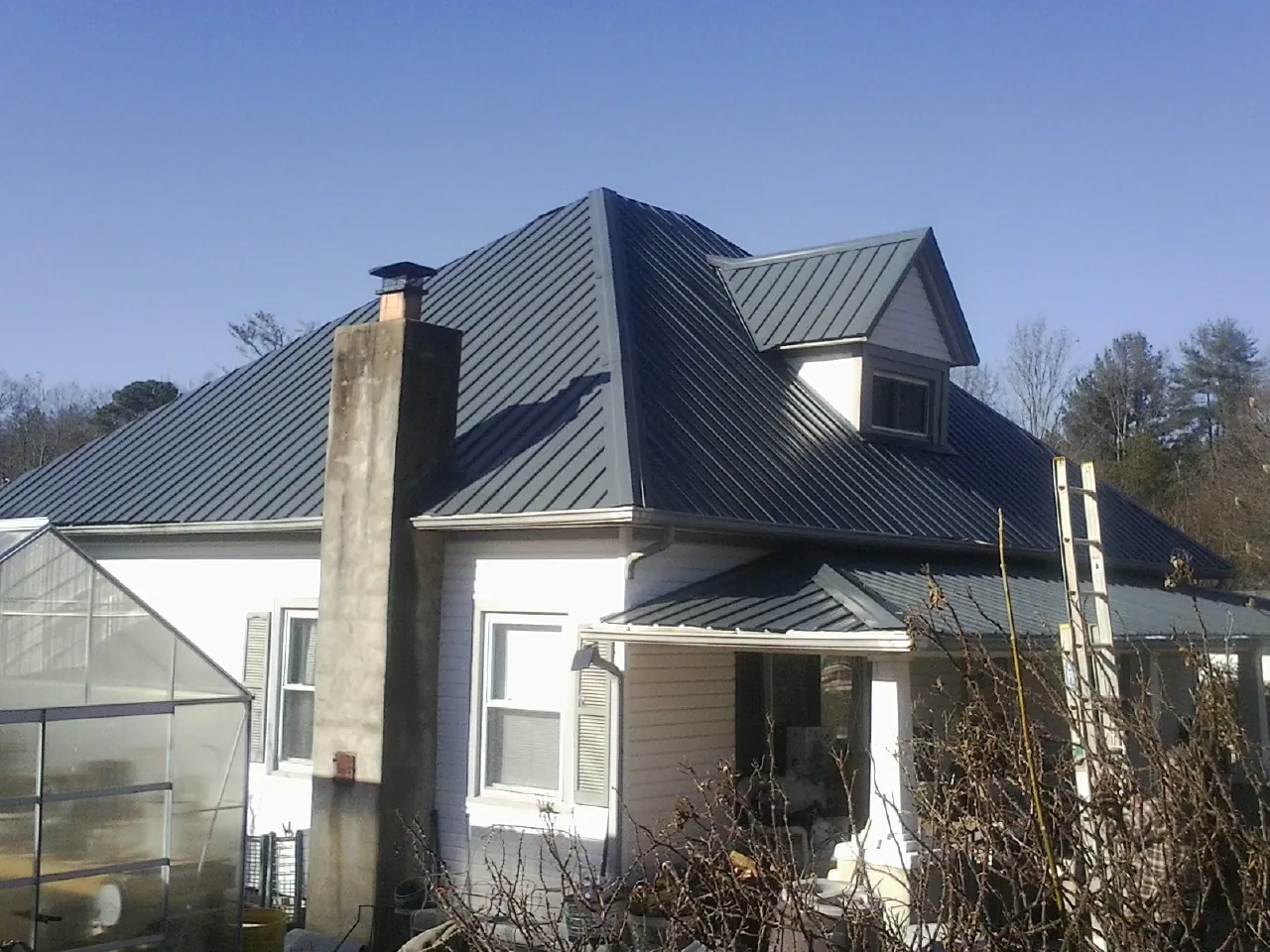 Dark blue standing seam metal roof on a white farmhouse with dormer — Slate & Tile Roof Repair by Roofing Brothers in Nathrop