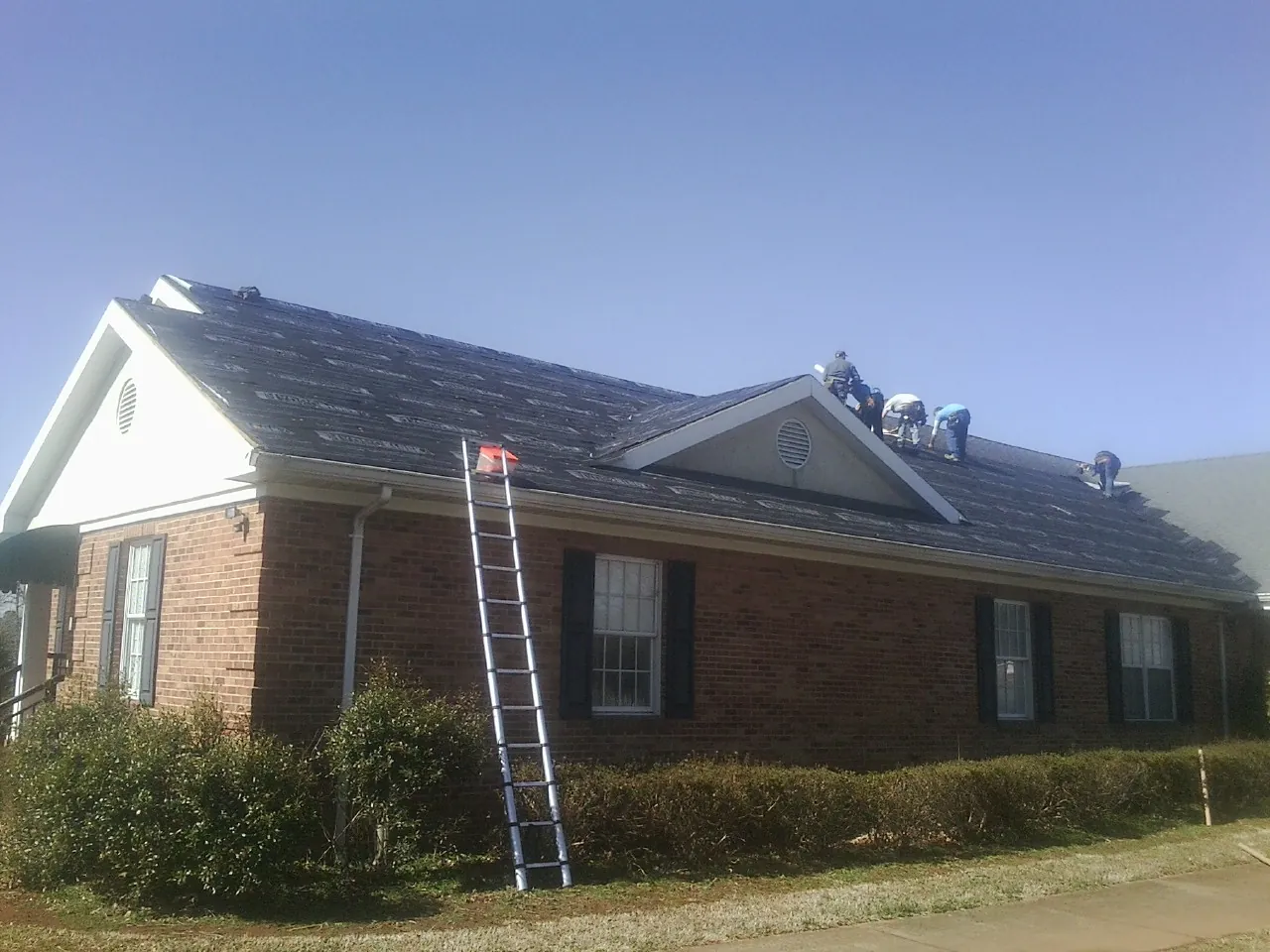 Crew tearing shingles off a brick ranch roof with a ladder set — Emergency Roof Repair work by our crew in Nathrop