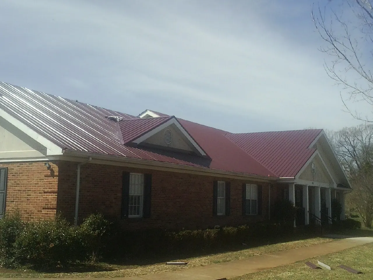 Red metal roof with gabled entries on a long brick building, from a Hail Damage Roof Repair job in Nathrop