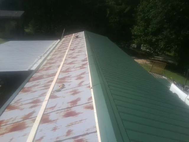 Old rusted panels beside newly installed green metal roofing — Wind Damage Roof Repair by Roofing Brothers in Nathrop