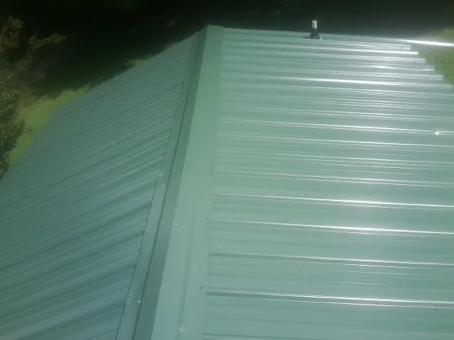 New green metal panels meeting at the ridge of a roof — Flat Roof Repair work by our crew in Nathrop