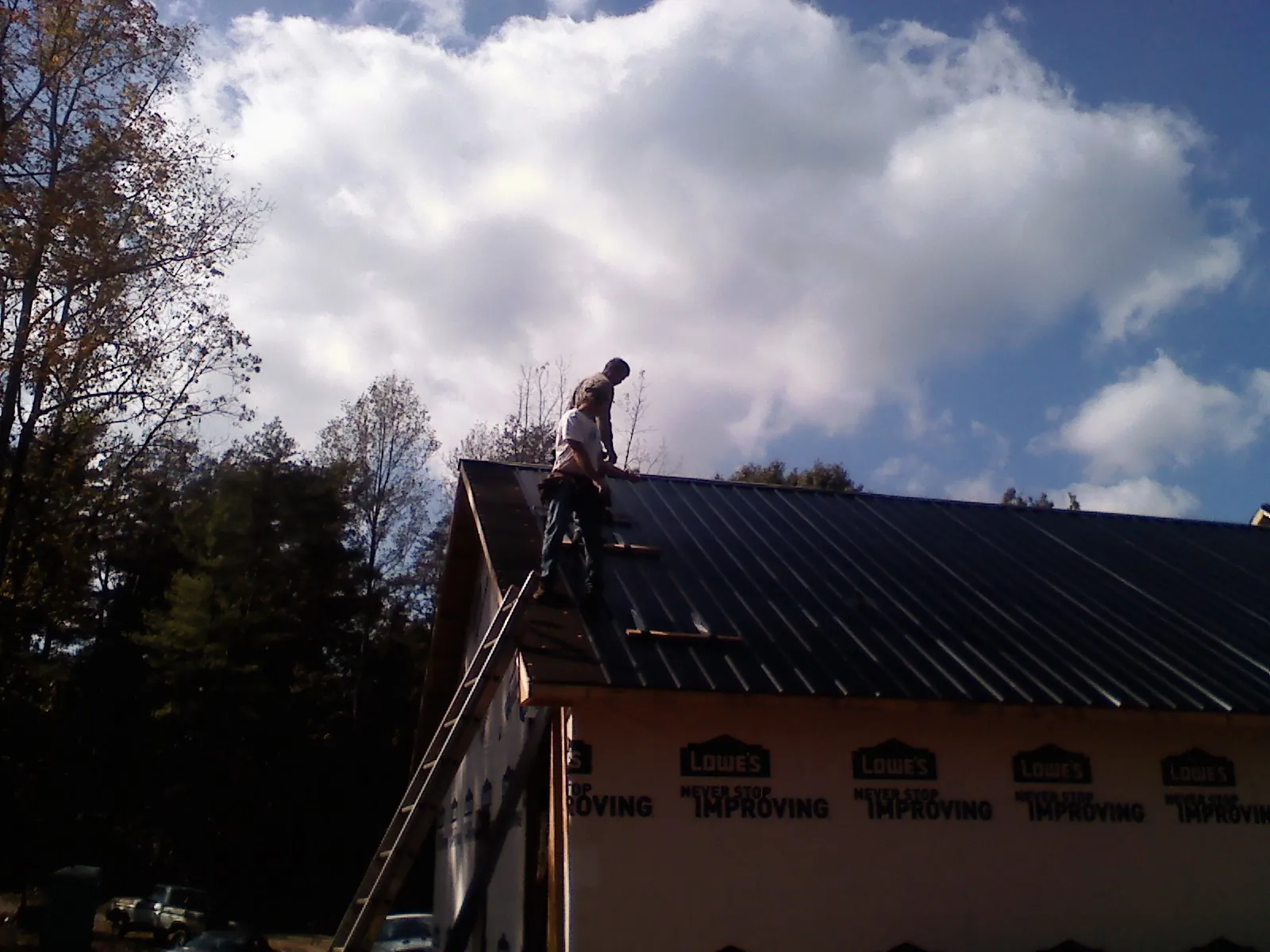 Roofer fastening dark metal panels high against a cloudy sky, from a Roof Inspection job in Nathrop