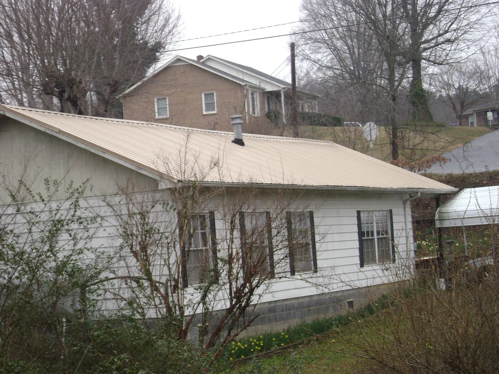 Tan metal roof on a white sided house set into a hillside — Commercial Roofing by Roofing Brothers in Nathrop